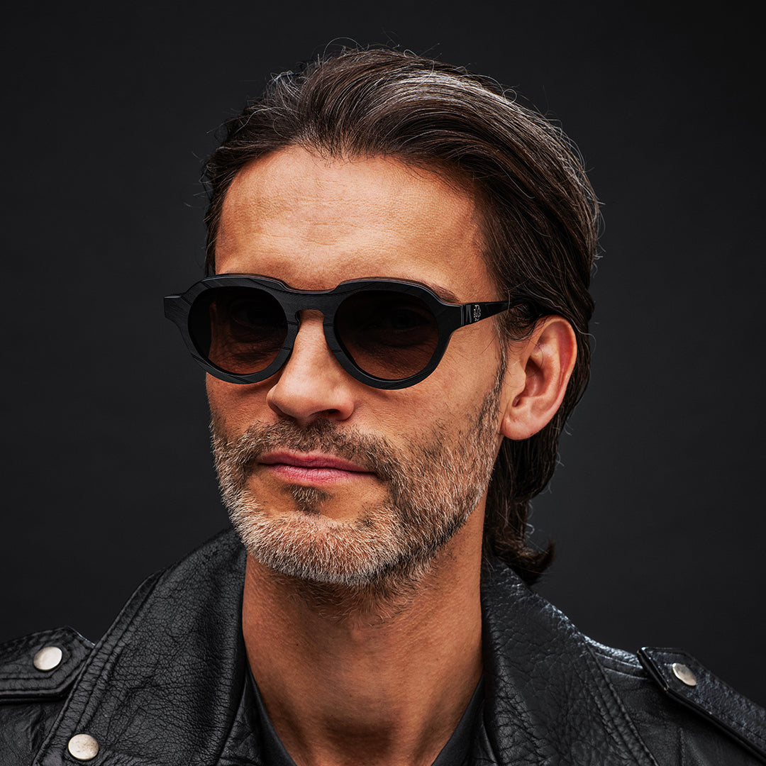 Man wearing black Vinylize Rammstein sunglasses and a black leather jacket against a dark background