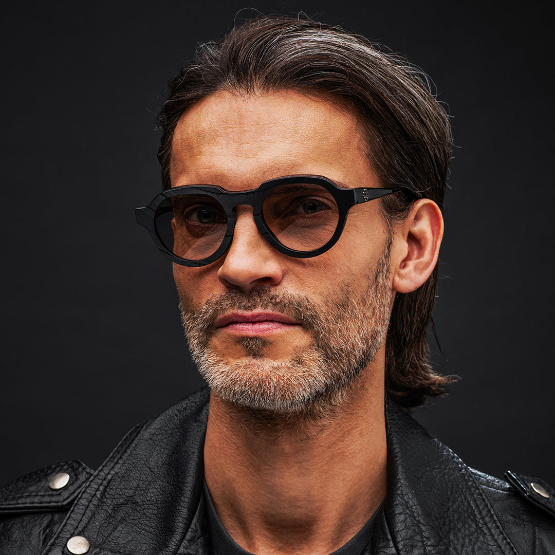 Man wearing black Vinylize Rammstein glasses and a black leather jacket against a dark background