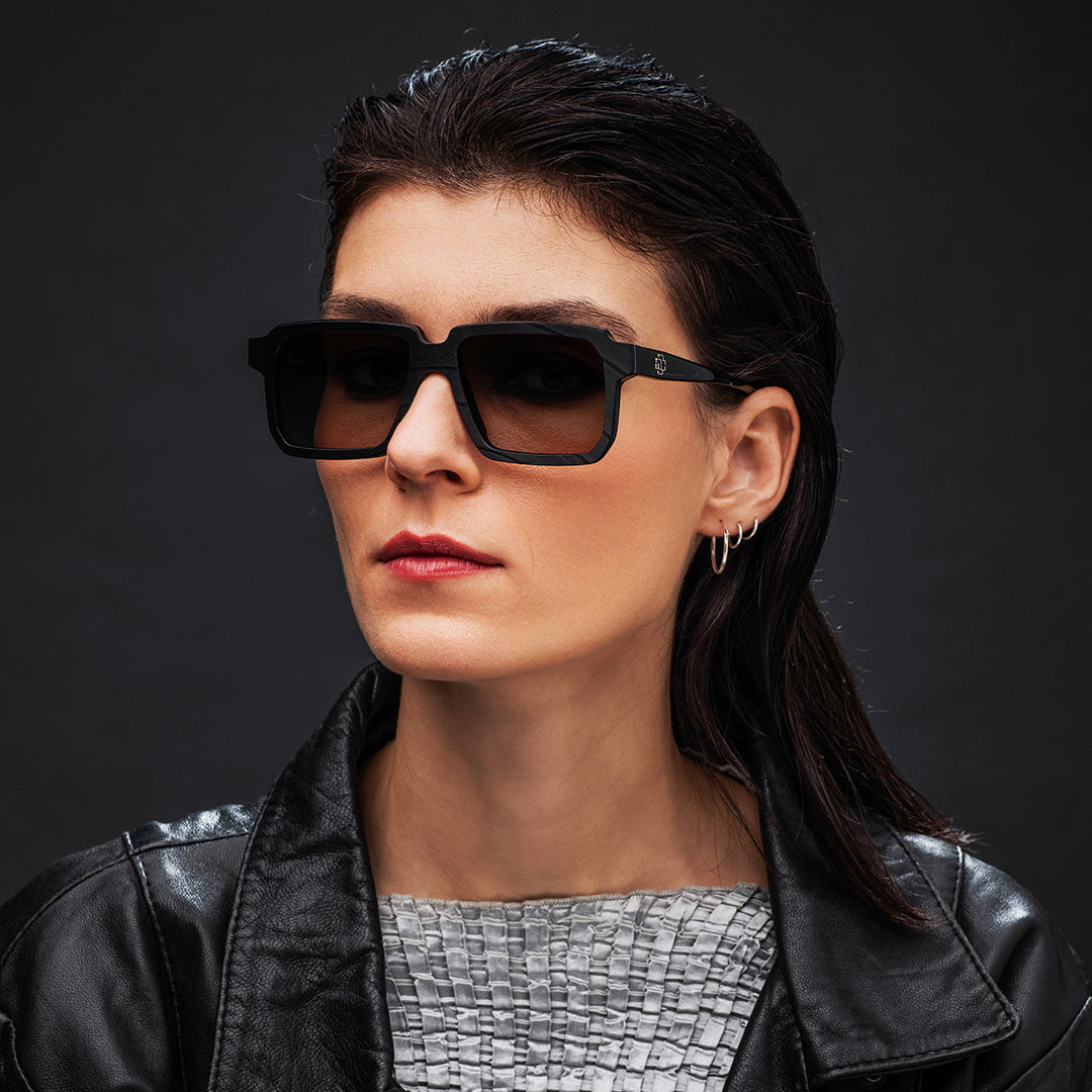 Woman wearing black Vinylize Rammstein sunglasses and a black leather jacket against a dark background