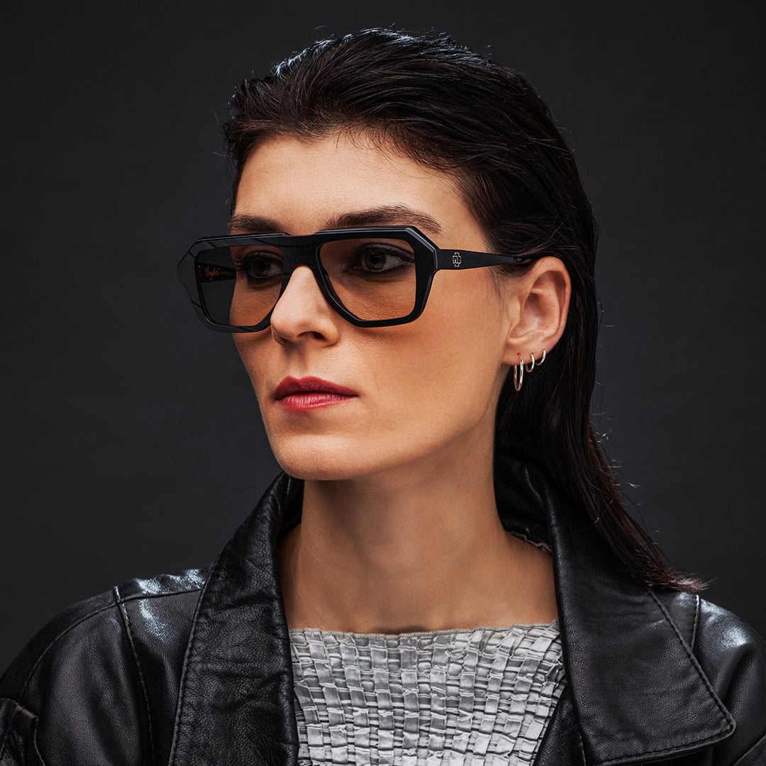 Woman wearing black Vinylize Rammstein glasses and a black leather jacket against a dark background