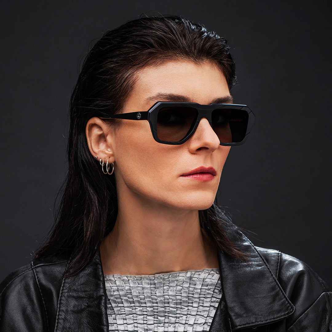 Woman wearing black Vinylize Rammstein sunglasses and a black leather jacket against a dark background