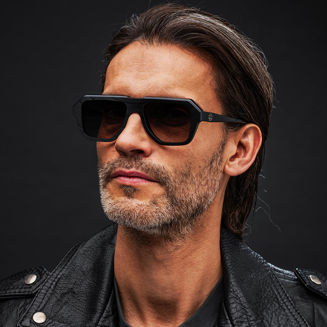 Man wearing black Vinylize Rammstein sunglasses and a black leather jacket against a dark background