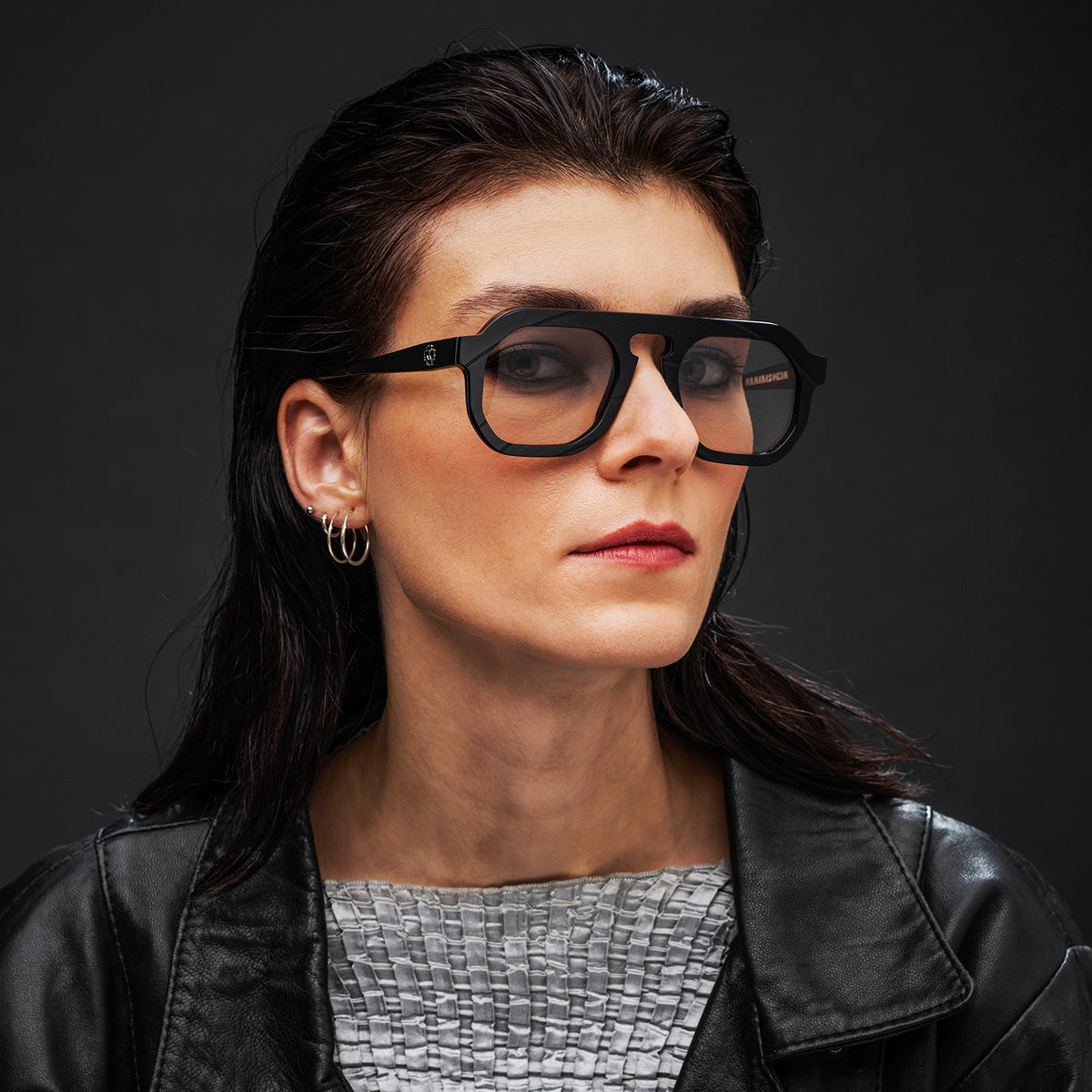 Woman wearing black Vinylize Rammstein glasses and a black leather jacket against a dark background