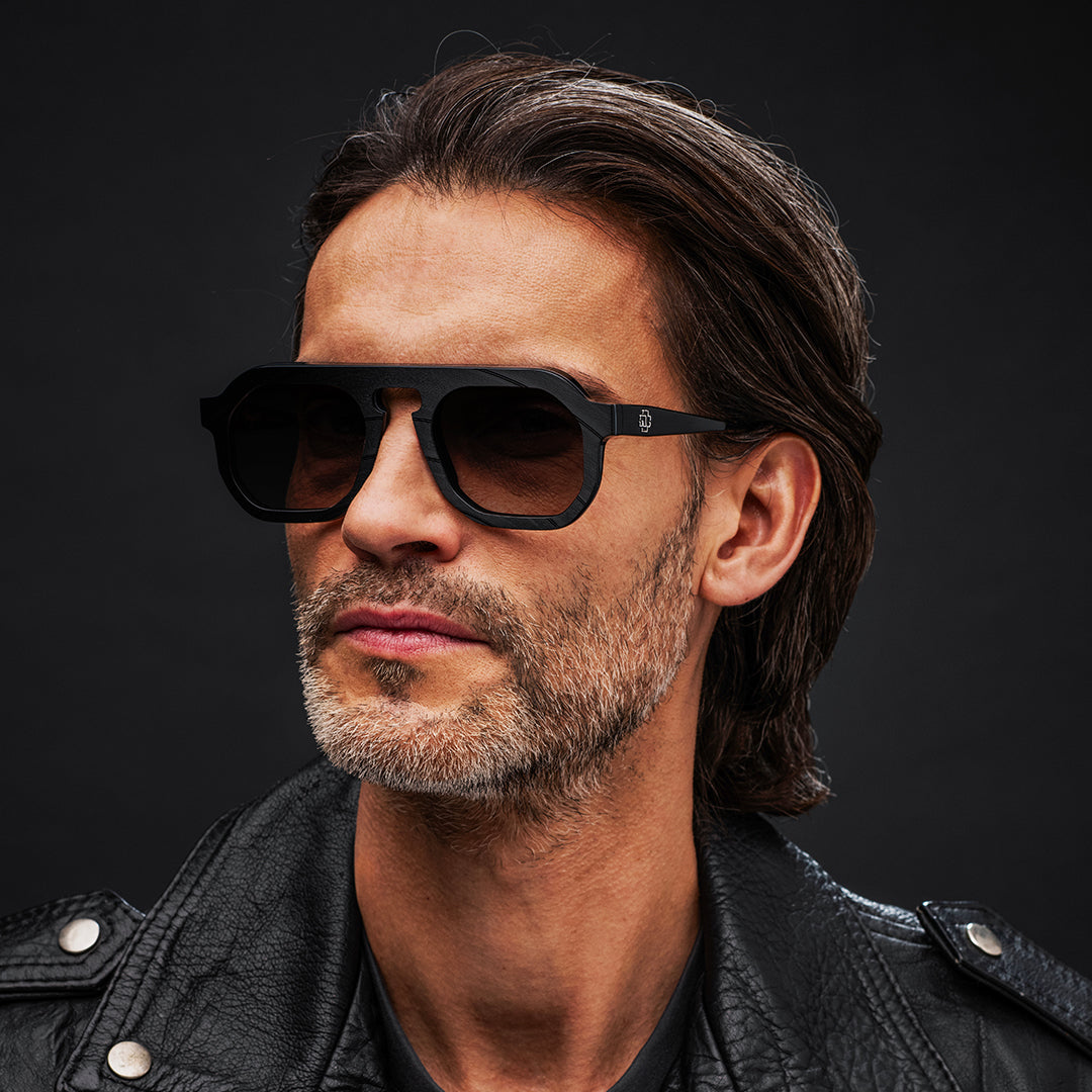 Man wearing Vinylize Rammstein sunglasses and a black leather jacket against a dark background