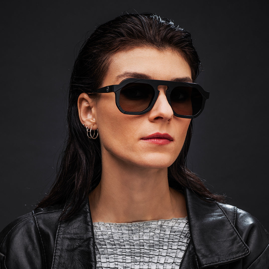 Woman wearing black Vinylize Rammstein sunglasses and a black leather jacket on a dark background