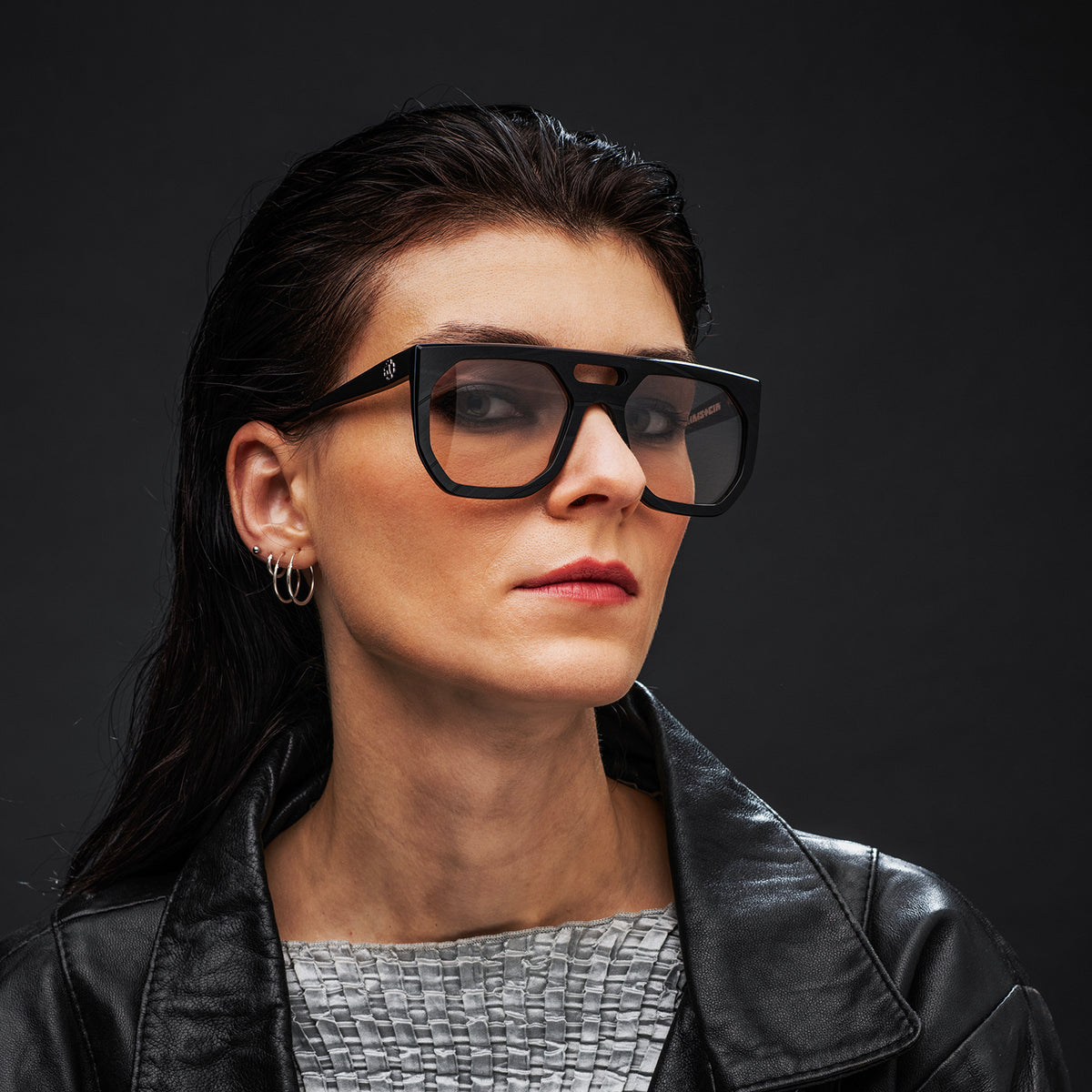 Woman wearing black Vinylize Rammstein glasses and a black leather jacket against a dark background