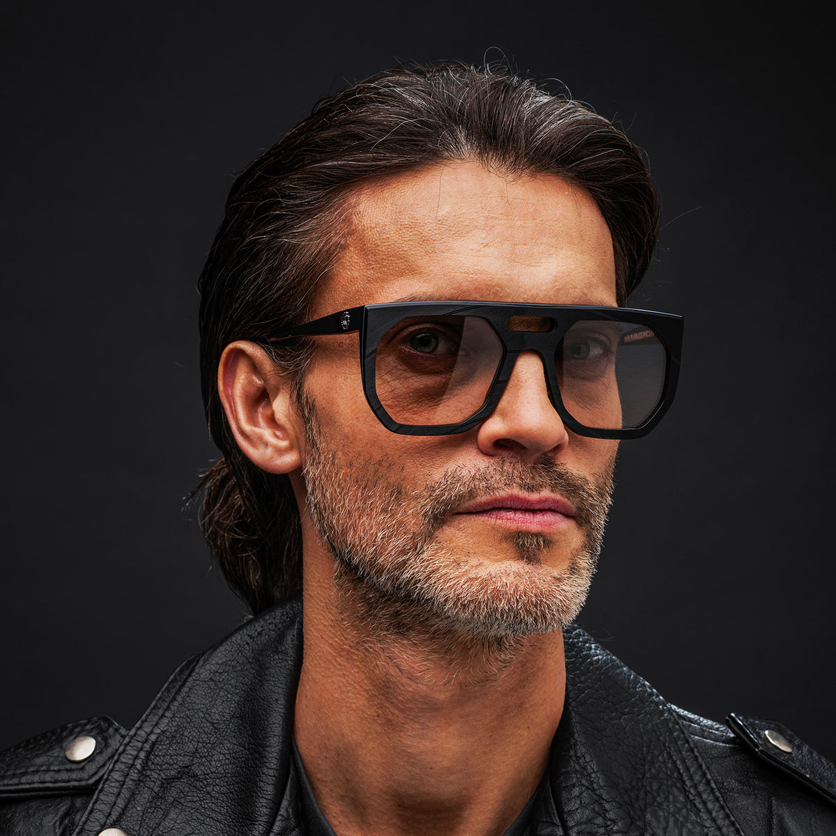 Man wearing black Vinylize Rammstein sunglasses and a leather jacket against a dark background