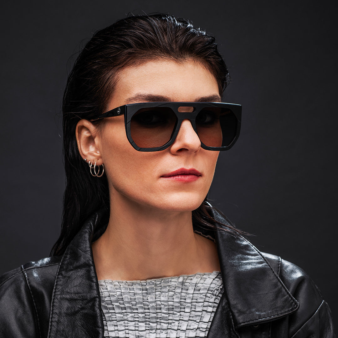 Woman wearing black Vinylize Rammstein sunglasses and a black leather jacket against a dark background